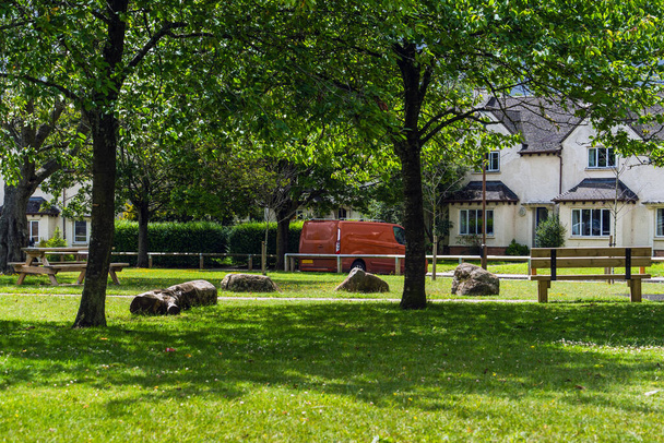 Idyllinen Englanti talo, rehevän vihreä nurmikko, pilkullinen auringonvalo puiden läpi, puinen penkki, vintage punainen auto, vanha talo seinät taustalla. - Valokuva, kuva