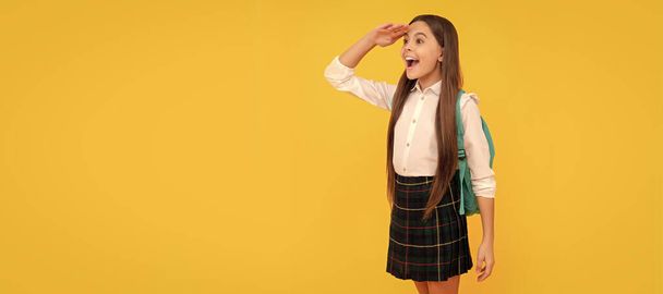 happy kid with backpack in school uniform full length on yellow background look far away, school. Horizontal isolated poster of school girl student. Banner header portrait of schoolgirl copy space - Foto, immagini