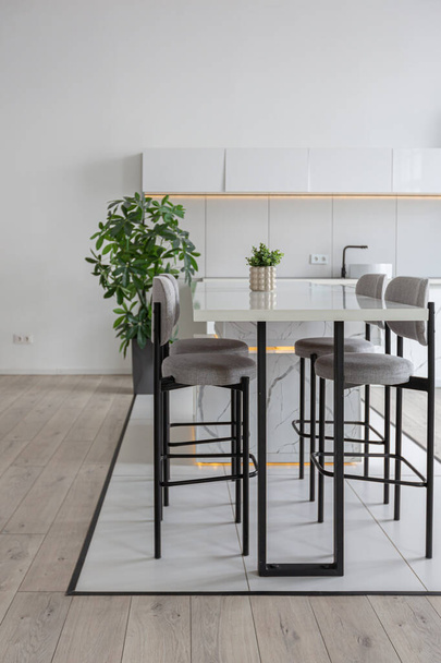 kitchen and dining island with high bar stools in a minimalistic modern luxury design of an expensive house on a sunny day. white walls with plaster, parquet, decorative lighting and no one inside - Foto, immagini