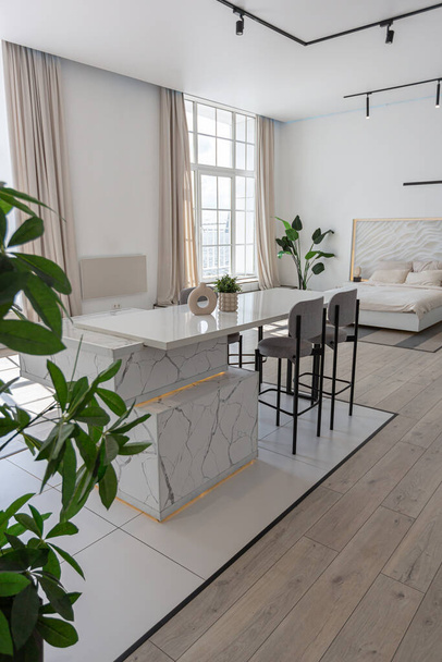 kitchen and dining island with high bar stools in a minimalistic modern luxury design of an expensive house on a sunny day. white walls with plaster, parquet, decorative lighting and no one inside - 写真・画像