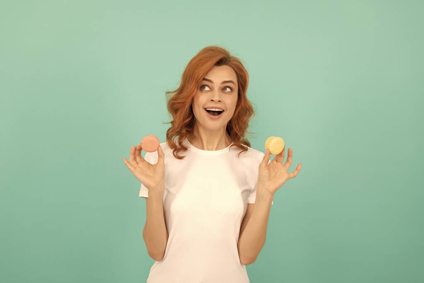 happy shocked woman hold sweet macaron french cookie on blue background. - Photo, Image