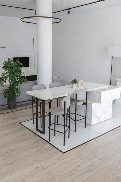 kitchen and dining island with high bar stools in a minimalistic modern luxury design of an expensive house on a sunny day. white walls with plaster, parquet, decorative lighting and no one inside - Valokuva, kuva