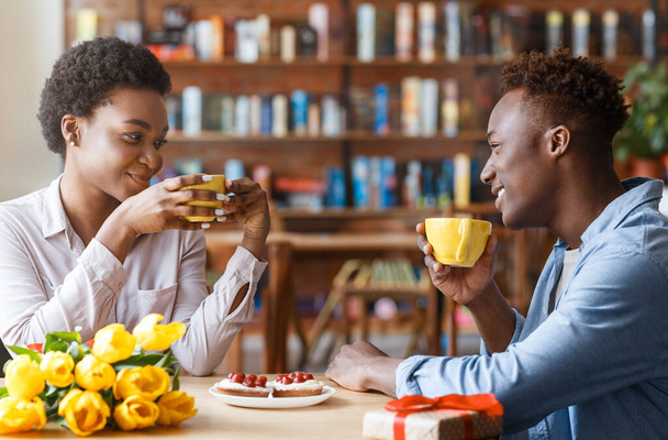 Adorabile felice giovane coppia nera hanno appuntamento romantico in caffetteria all'ora di pranzo. Bella donna afroamericana millenaria che racconta al suo ragazzo come è andata la sua giornata, seduti insieme al caffè - Foto, immagini