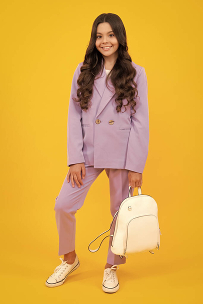 School girl in school uniform with school bag. Schoolchild teenager hold backpack on yellow isolated background. Happy teenager, positive and smiling emotions of teen girl - Fotó, kép