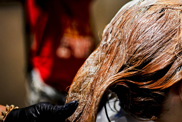 zbliżenie fryzjera nakłada farbę pędzlem na jasnoczerwone pasma włosów z rękawiczkami. Farbowanie włosów - Zdjęcie, obraz