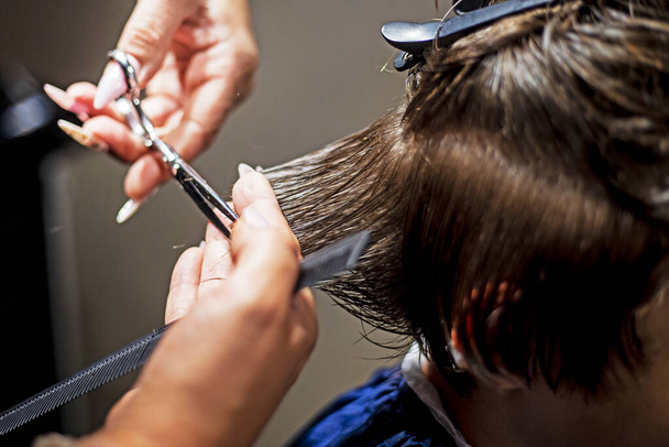 Kuaför koyu sarı saçlı tenager bir çocuk için şık bir saç kesimi yapıyor. - Fotoğraf, Görsel
