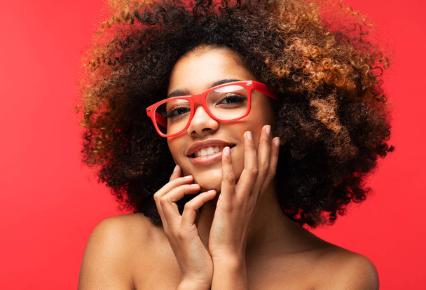 Portrait of Young African female model wearing eyeglasses over red color background - Zdjęcie, obraz