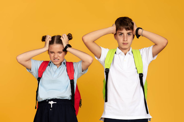 Sad angry tired teen european boy and girl with backpacks cover ears with hands, isolated on yellow studio background. Friendship, childhood, problems in education at school, bullying, noise - Foto, immagini