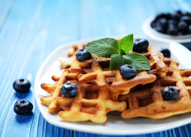 Waffles with blueberries and raspberries for breakfast on white plate over blue wooden table. Close up. - Photo, image