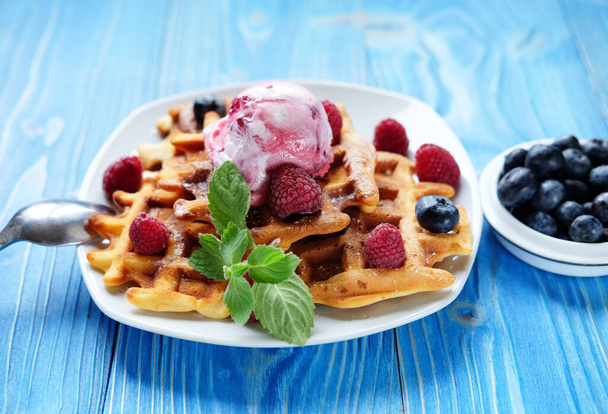 Waffles with ice cream and raspberries for breakfast over blue wooden table. Close up. - Photo, image