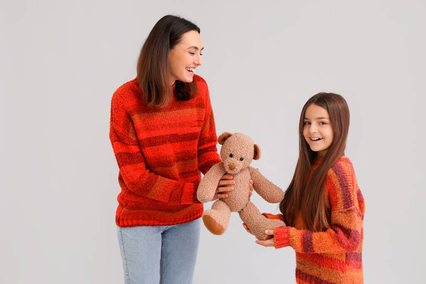 Bambina e sua madre in maglioni caldi con orso giocattolo su sfondo grigio - Foto, immagini
