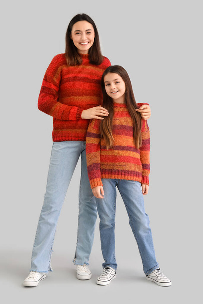 Klein meisje en haar moeder in warme truien op grijze achtergrond - Foto, afbeelding