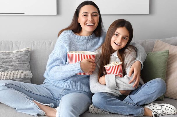 Küçük kız ve annesi sıcak kazak giyip evde patlamış mısır izleyip televizyon izliyorlar. - Fotoğraf, Görsel