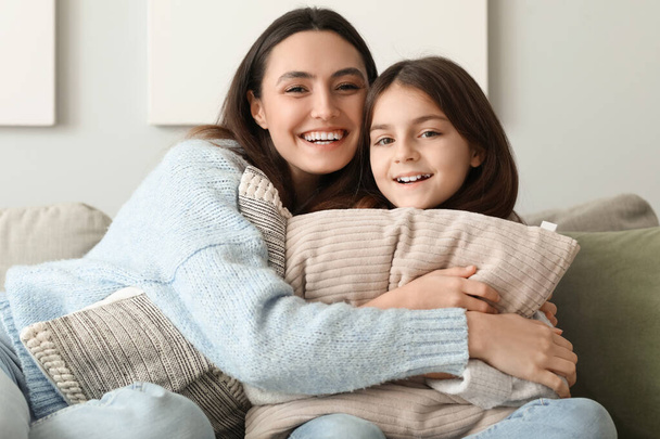 Klein meisje en haar moeder in warme truien met kussens zitten op de bank thuis - Foto, afbeelding
