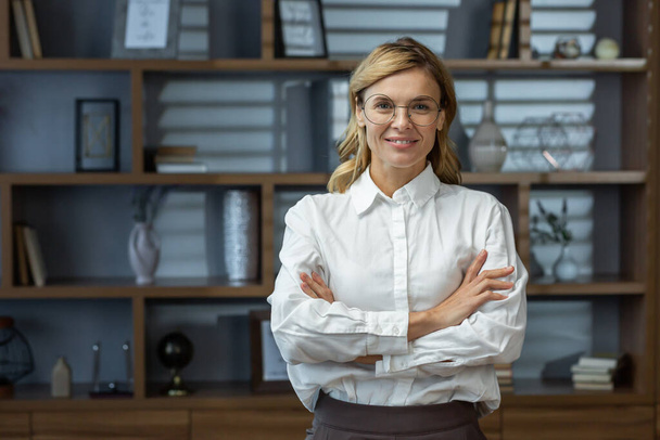 Portrait of mature experienced female boss, senior woman smiling and looking at camera with crossed arms, business woman in business shirt, financier inside office successful. - Photo, Image