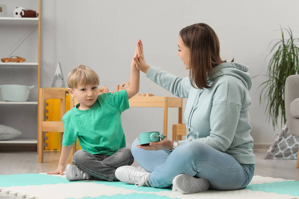 Nanny with alarm clock and little boy giving each other high-five at home - Foto, Bild