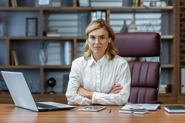 Portrait of serious mature woman inside office at workplace, businesswoman thoughtfully in glasses looking at camera with arms crossed. - Фото, зображення