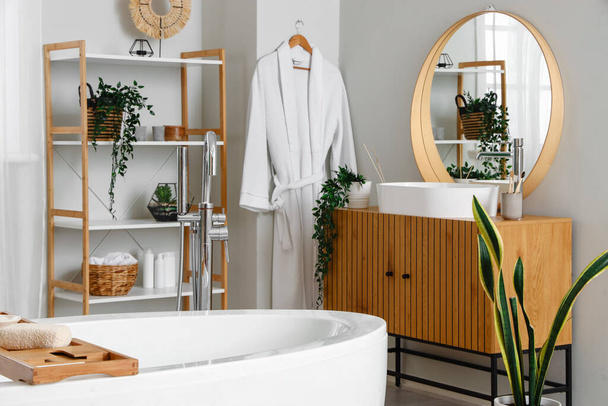 Interior de baño de luz con bañera, armario de madera y espejo - Foto, imagen