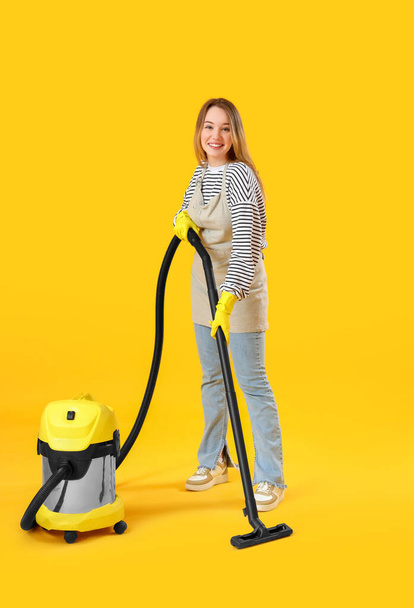 Jeune femme avec aspirateur sur fond jaune - Photo, image