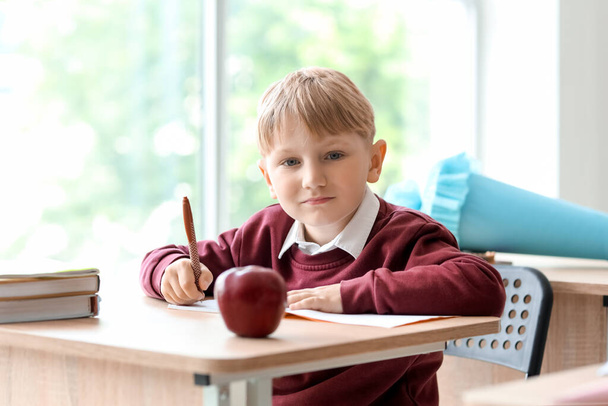 Menino feliz com cone de escola azul sentado na mesa em sala de aula - Foto, Imagem