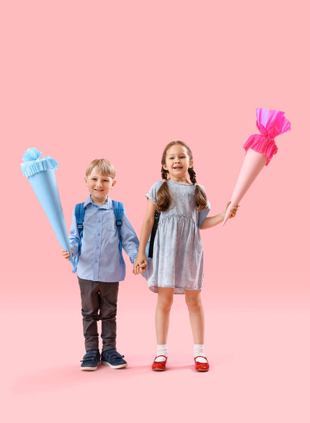 Happy little classmates with backpacks and colorful school cones on pink background - Foto, afbeelding