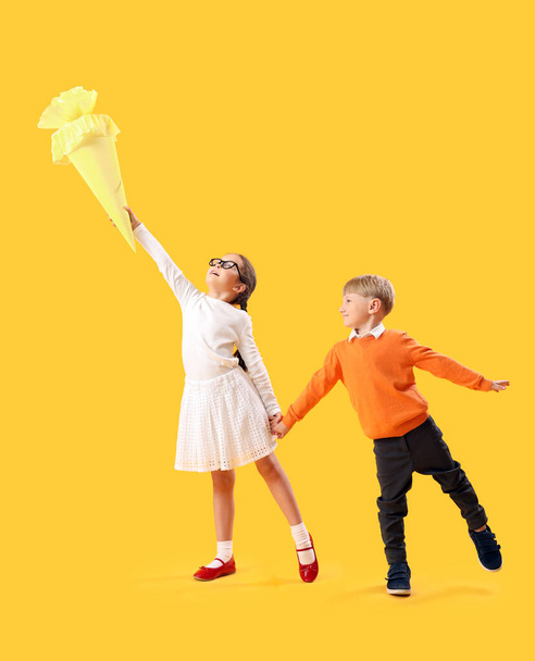Щаслива маленька дівчинка і хлопчик зі шкільним конусом стрибає на жовтому тлі - Фото, зображення
