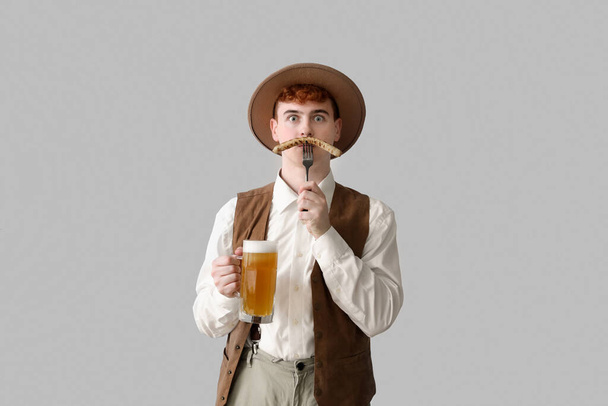 Young man in traditional German clothes with beer and sausage on light background - Foto, immagini