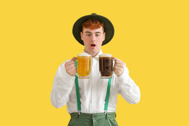 Shocked young man in traditional German clothes with beer on yellow background - Foto, imagen