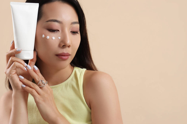 Hermosa mujer asiática con crema facial sobre fondo beige - Foto, imagen