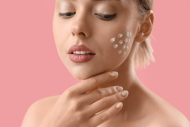 Pretty young woman with cream on her face against pink background - Photo, Image