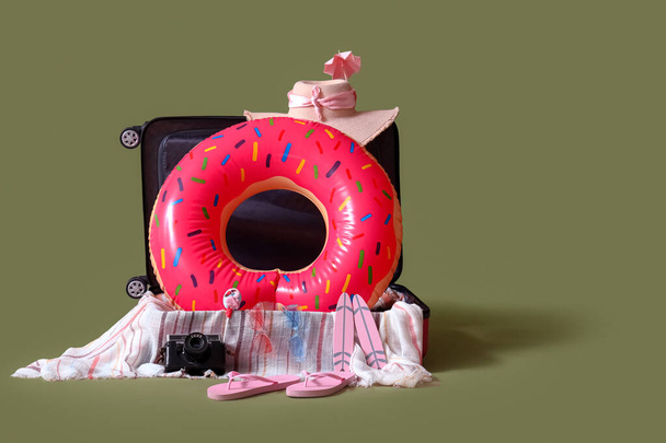 Suitcase with inflatable ring in shape of donut and beach accessories on green background. Travel concept - Photo, image
