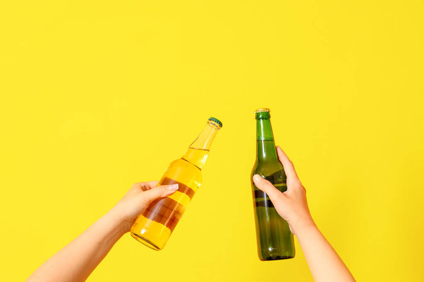 Female hands with cold beer clinking on yellow background - Фото, зображення