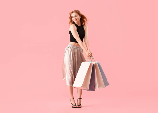 Beautiful happy young woman with shopping bags on pink background - Фото, зображення
