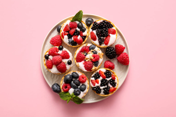 Plate of tasty tartlets with whipped cream and berries on pink background - Photo, Image