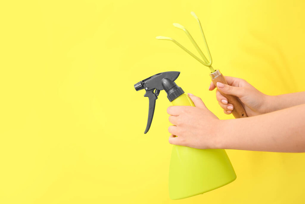 Woman with gardening rake and water spray on yellow background - Photo, Image