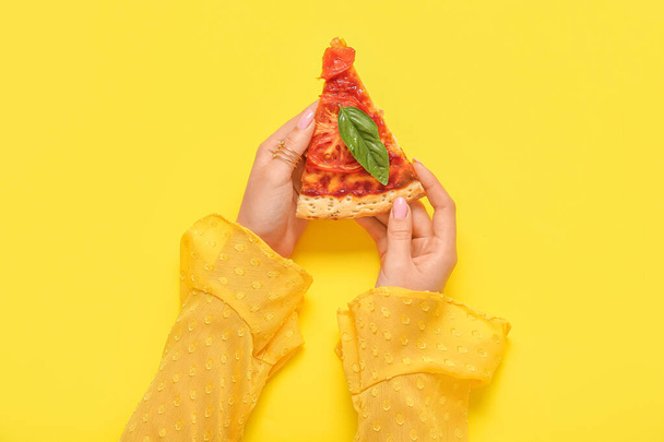 Woman holding slice of tasty pizza on yellow background - Fotografie, Obrázek