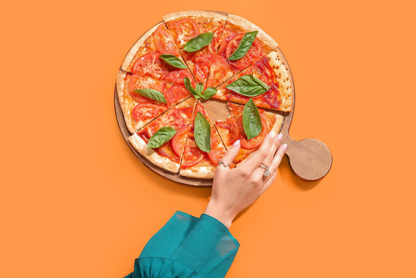 vrouw nemen slice van smakelijke pizza op oranje achtergrond - Foto, afbeelding