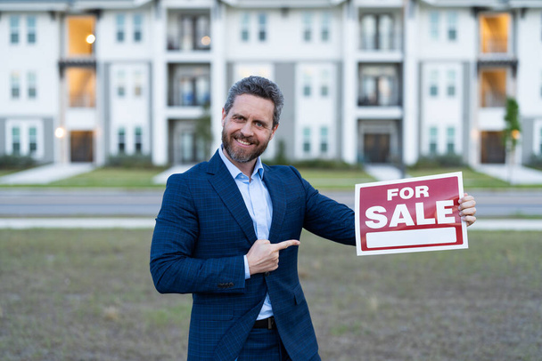 photo of broker with for sale board, point finger. sale property by broker. man broker hold board for sale property. sale property by broker outdoor. - Photo, Image
