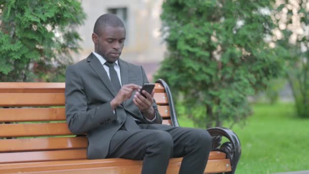 Afričtí podnikatelé procházení Smartphone zatímco sedí venku - Záběry, video