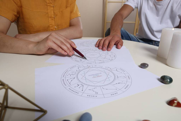 Astrologer showing natal charts to client at table indoors, closeup - Фото, зображення