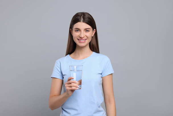 Healthy habit. Portrait of happy woman holding glass with fresh water on grey background - Photo, image