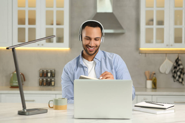 Young man with headphones working on laptop at desk in kitchen. Home office - Foto, Imagem