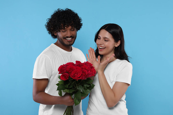 International dating. Handsome man presenting roses to his beloved woman on light blue background - Foto, imagen