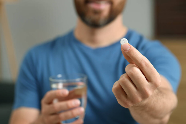 Man with glass of water and pill on blurred background, closeup - Fotoğraf, Görsel