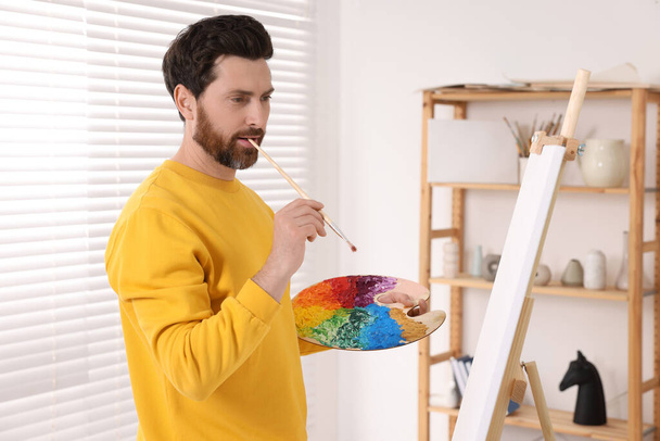 Man painting in studio. Using easel to hold canvas - Foto, Imagem