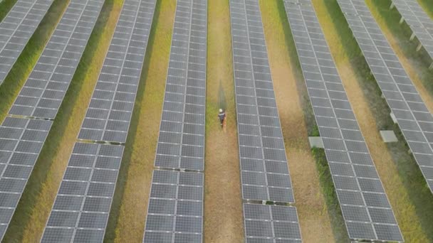 Bovenaanzicht van de werknemer lopen in zonne-energie boerderij om het controleren van zonnepaneel. ingenieurs inspecteert de bouw van zonnecellen paneel. Drone vlucht vliegen over zonnepanelen veld hernieuwbare groene alternatieve energie. - Video