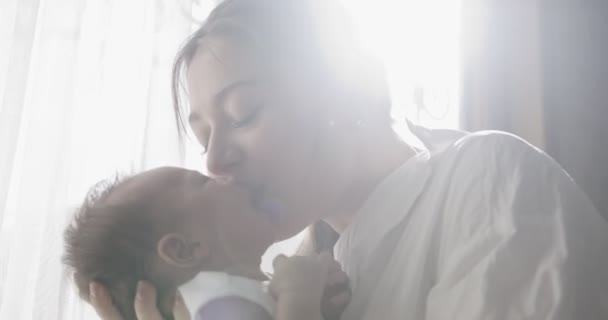 Moeder met wit shirt houdt baby op handen. Een close-up. Binnenschot. Raam met witte gordijnen aan de achterkant - Video