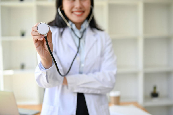 lähikuva ammattilaisesta aasialaisesta naislääkäristä valkoisessa puvussa, jolla on stetoskooppi seistessään tutkimushuoneessaan sairaalassa. - Valokuva, kuva