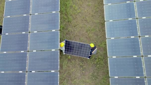 Vue du dessus d'un travailleur tenant un panneau solaire et marchant dans une ferme solaire. ingénieurs inspecte la construction de panneaux solaires. Vol de drone survoler les panneaux solaires champ renouvelable énergie verte alternative. - Séquence, vidéo