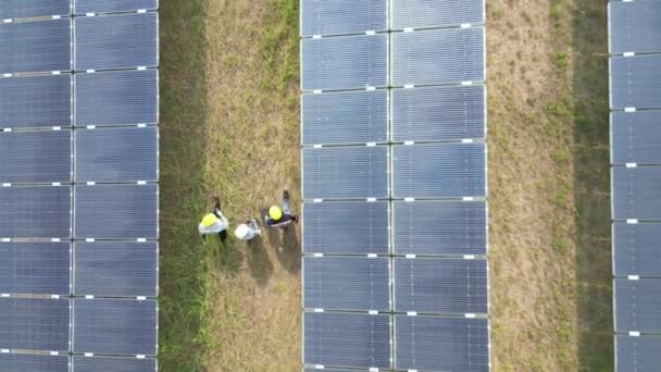 Вид сверху на инженеров, проверяющих солнечные панели и прогуливающихся по солнечной ферме. инженеры осматривают строительство панели солнечных батарей. Полет беспилотника над полем солнечных батарей возобновляемые источники зеленой энергии. - Кадры, видео
